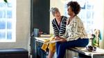 Due donne sedute su un piano di lavoro mentre parlano e ridono