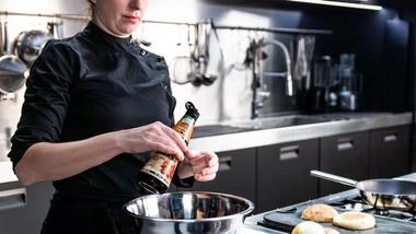 Cuoca in una cucina professionale mentre versa una bottiglia di Knorr Intense Flavours in una ciotola.