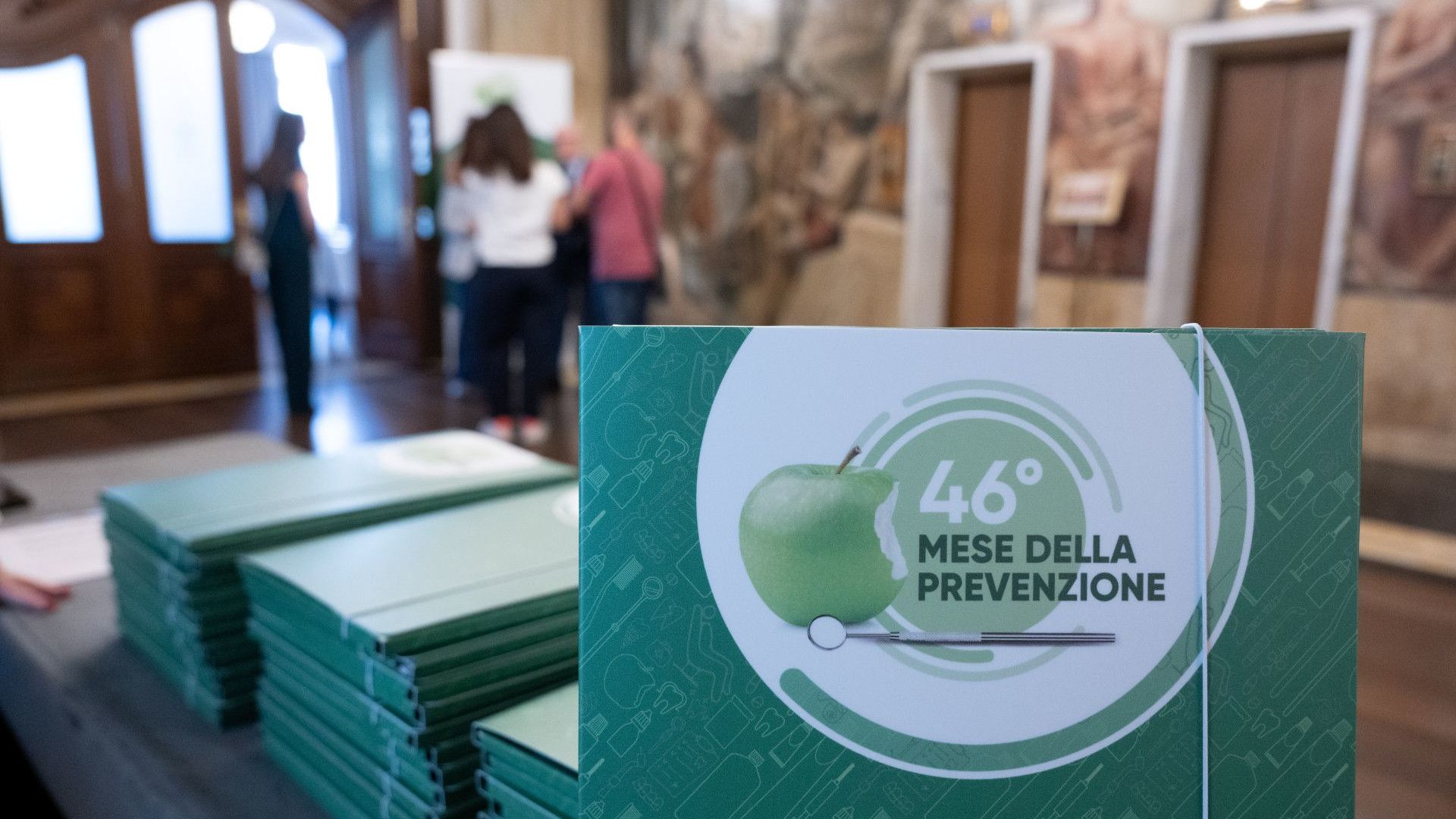 Cartella stampa cartacea verde con logo del 46° Mese della Prevenzione dentale di Mentadent e Andi, con sfondo alla conferenza stampa