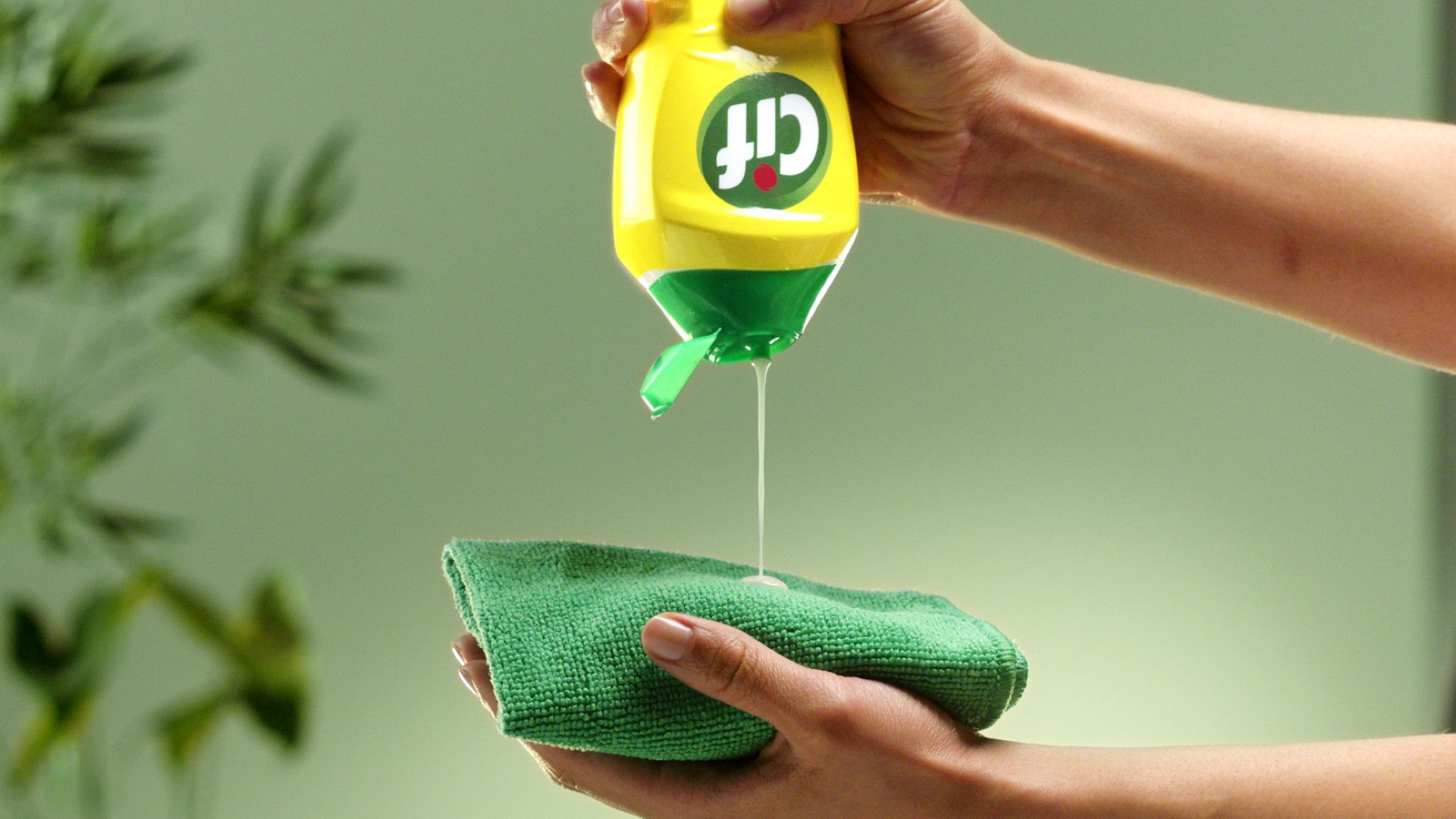 Persona che versa detergente liquido da una bottiglia gialla su un panno verde per la pulizia