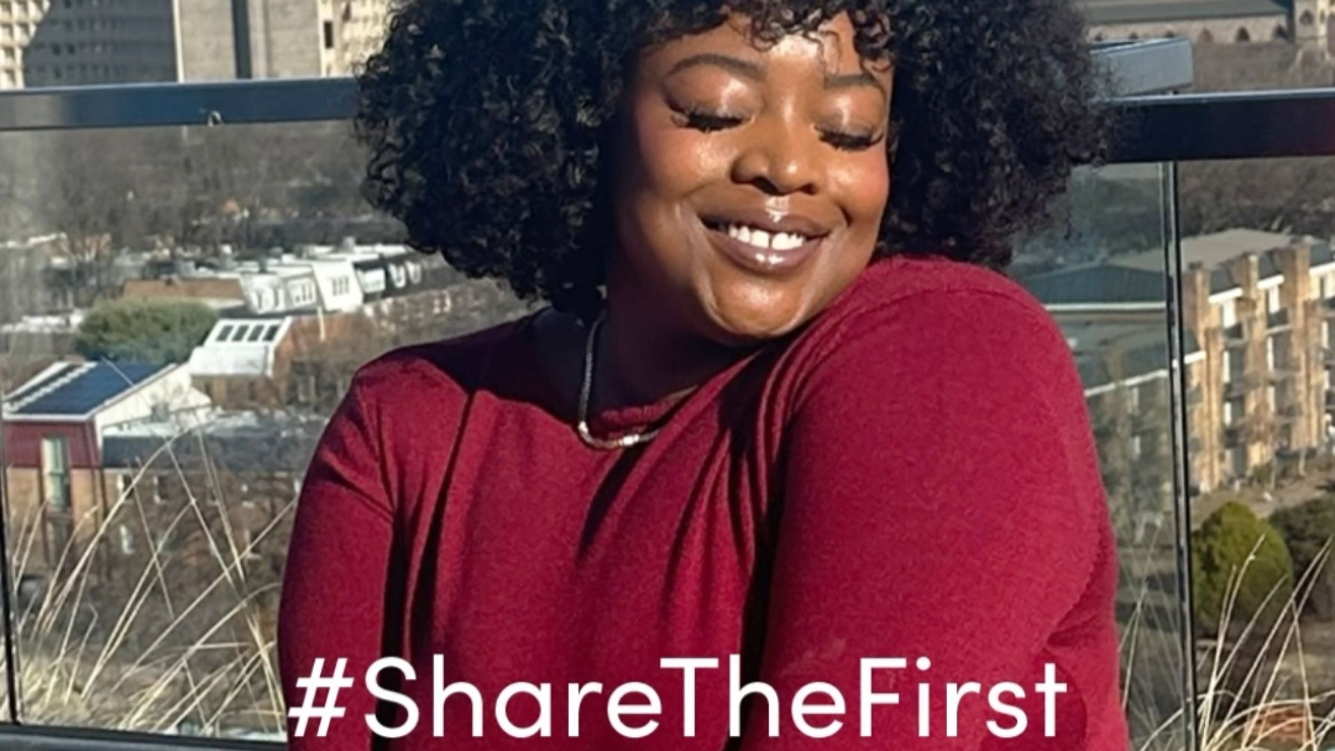 Un selfie di una donna con un vestito rosso e capelli scuri e ricci con lo slogan #ShareTheFirst