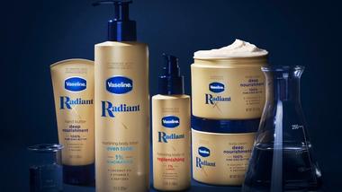 Prodotti della collezione Vaseline Radiant X, tra cui la Nourishing Body Lotion e l’Hydrating Body Oil. Il packaging è dorato su sfondo blu scuro.
