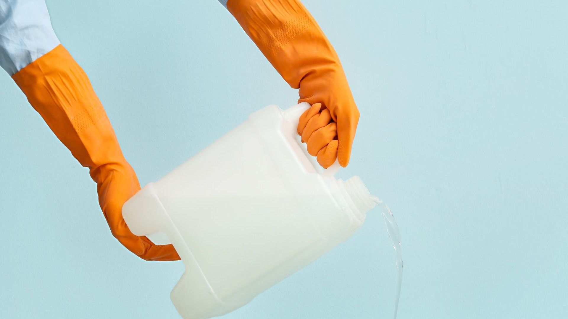 Mani con guanti gialli che tengono una tanica di plastica vergine con un prodotto per la pulizia della casa.